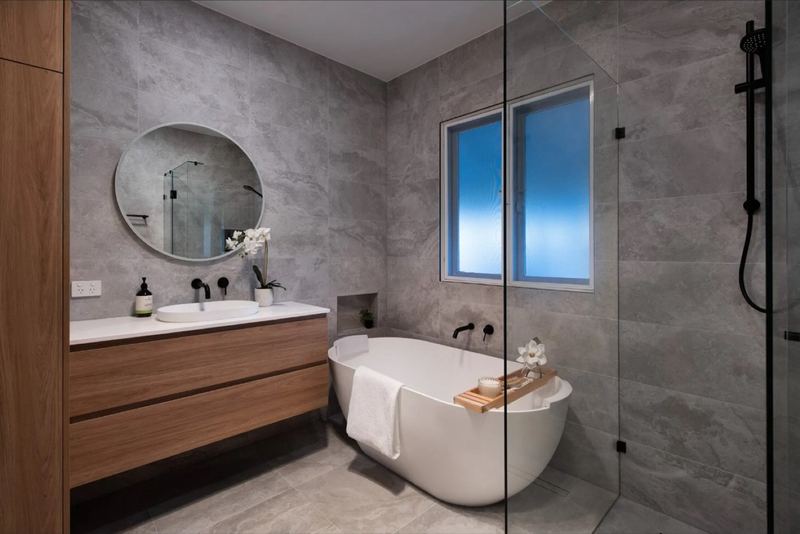 Bathroom with grey stone-look tiles, freestanding bath, round mirror and timber vanity