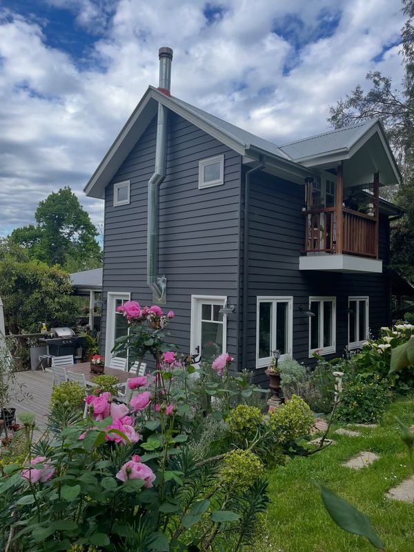 Dark grey weatherboard two-storey home with a timber balcony and a garden of pink roses